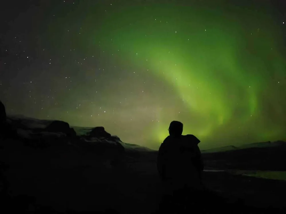 A silhouette watching green aurora over a dark landscape.