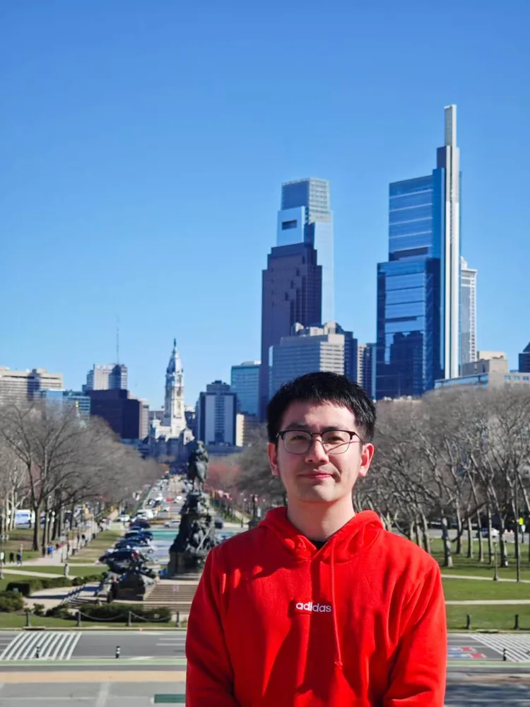 Ethan in a red hoodie with a city boulevard and skyline in the background.