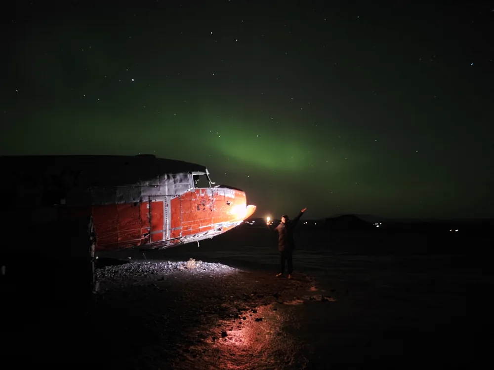 A person beside an aircraft fuselage under the night sky and aurora.