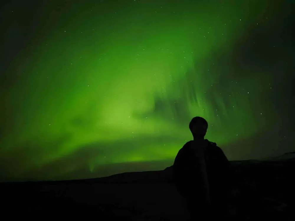 A silhouette beneath a bright green aurora.