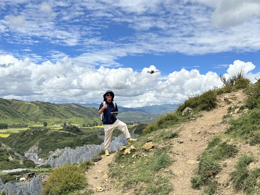 Ethan on a hillside trail beneath a blue sky, with a drone overhead.