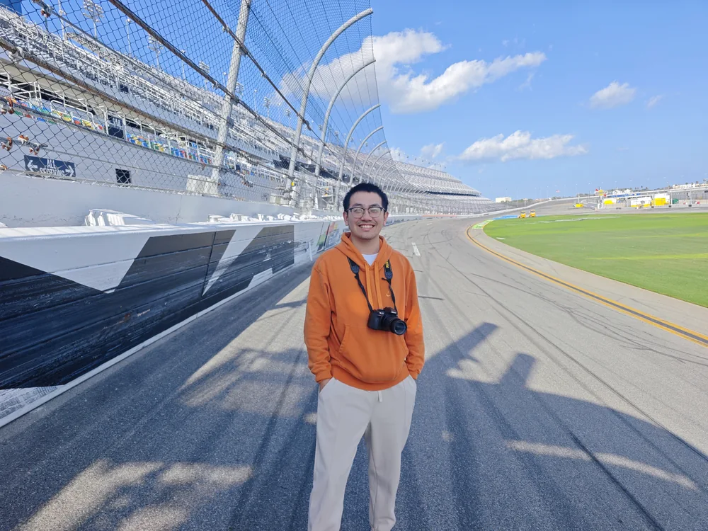 Ethan with a camera standing beside a motor racing track.